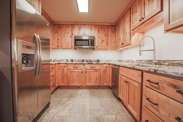 kitchen featuring light brown cabinets, a sink, appliances with stainless steel finishes, and light stone countertops