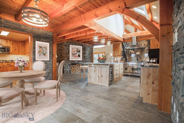 kitchen featuring a breakfast bar area, beamed ceiling, stainless steel appliances, wooden ceiling, and wall chimney range hood