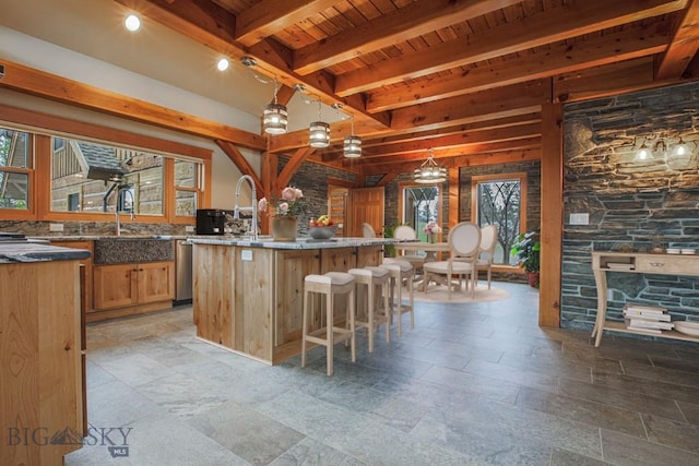 kitchen featuring beamed ceiling, a center island with sink, pendant lighting, a breakfast bar, and wooden ceiling