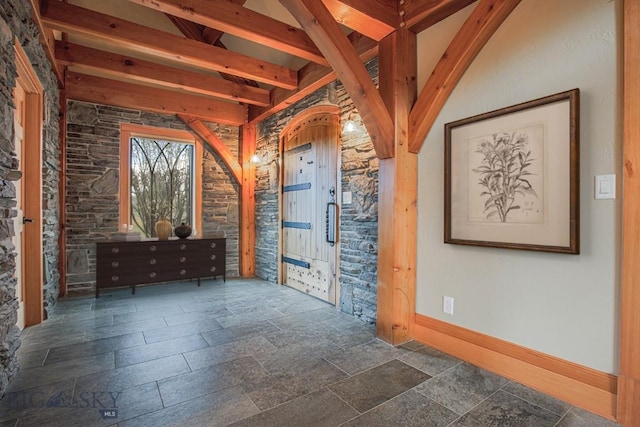 interior space with lofted ceiling with beams, arched walkways, baseboards, and stone tile flooring