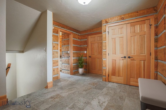 hallway featuring rustic walls, an upstairs landing, stone finish floor, and a textured ceiling