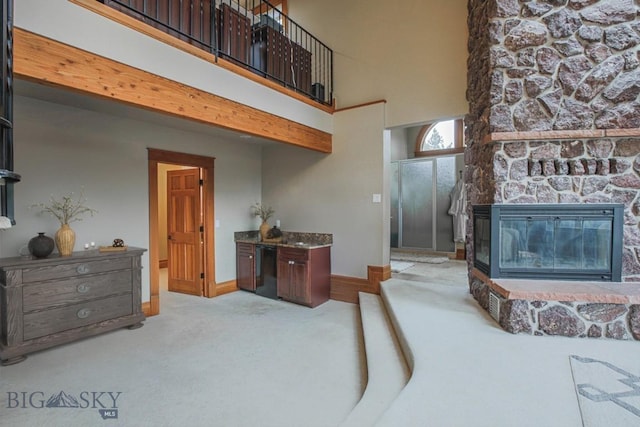 interior space with a stone fireplace, baseboards, a towering ceiling, and carpet floors