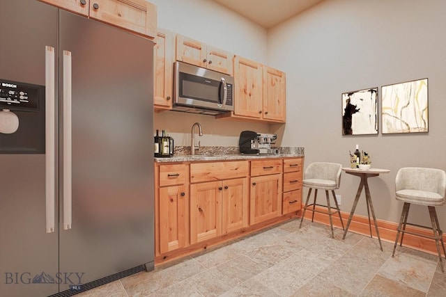 kitchen with light stone counters, baseboards, a sink, light brown cabinetry, and stainless steel appliances