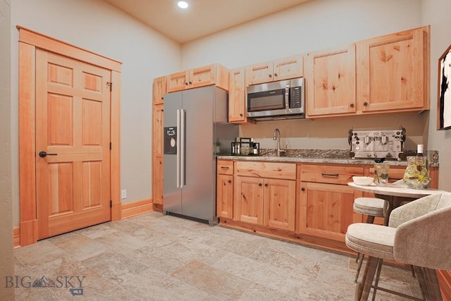 kitchen with light brown cabinetry, baseboards, stainless steel appliances, and light stone counters