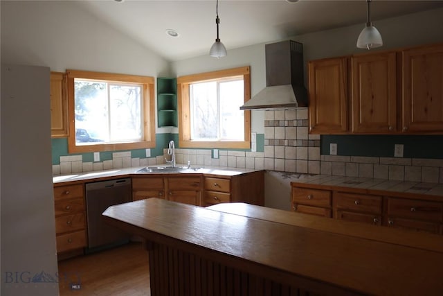 kitchen with lofted ceiling, a sink, stainless steel dishwasher, wall chimney range hood, and decorative light fixtures