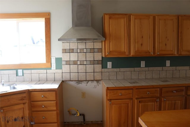 kitchen featuring decorative backsplash, tile countertops, wall chimney exhaust hood, and a sink