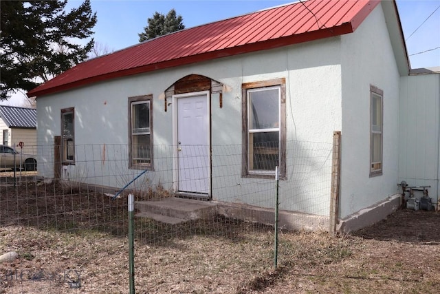 exterior space featuring stucco siding, fence, and metal roof