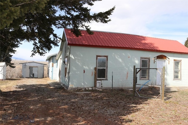 back of house with an outdoor structure, a storage unit, and metal roof