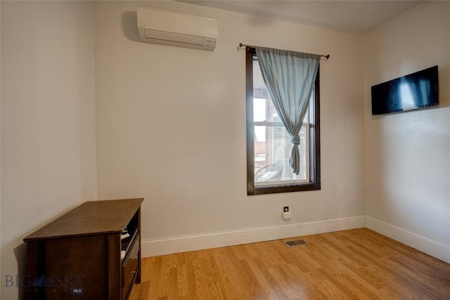 unfurnished room with baseboards, light wood-type flooring, and a wall mounted AC