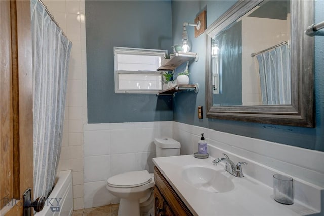 full bathroom featuring vanity, a wainscoted wall, shower / bath combo with shower curtain, tile walls, and toilet