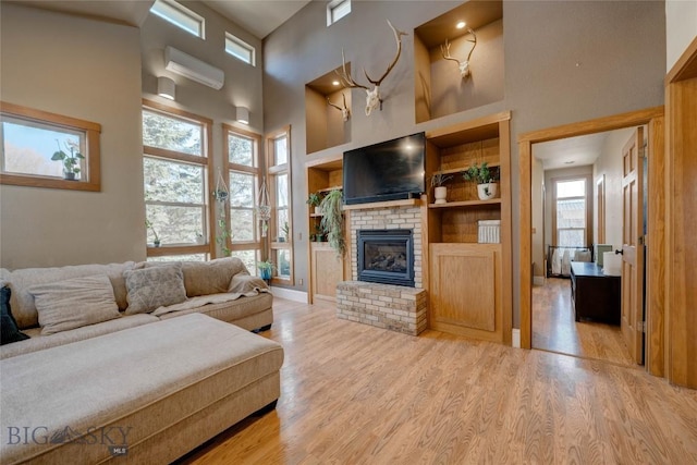 living area with built in shelves, an AC wall unit, light wood-style flooring, a fireplace, and a towering ceiling