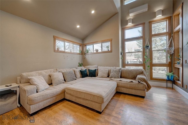 living room featuring a wall unit AC, baseboards, high vaulted ceiling, light wood-style flooring, and recessed lighting