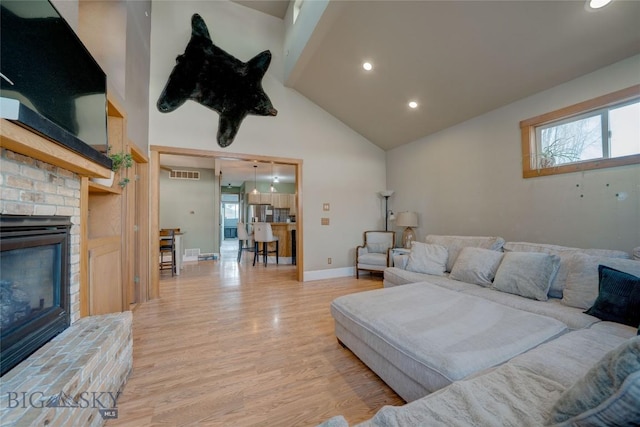 living room featuring visible vents, high vaulted ceiling, light wood-style flooring, a fireplace, and baseboards