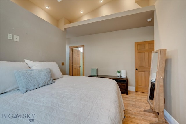 bedroom featuring baseboards, light wood finished floors, and high vaulted ceiling