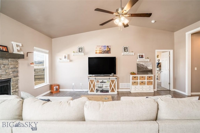 living room with a stone fireplace, vaulted ceiling, wood finished floors, and visible vents