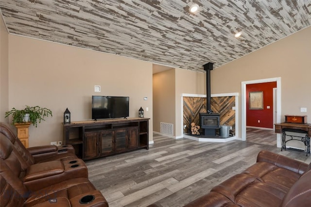 living room featuring visible vents, wood finished floors, baseboards, lofted ceiling, and a wood stove