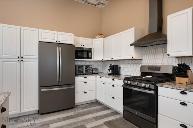 kitchen with light stone counters, appliances with stainless steel finishes, white cabinetry, and wall chimney range hood