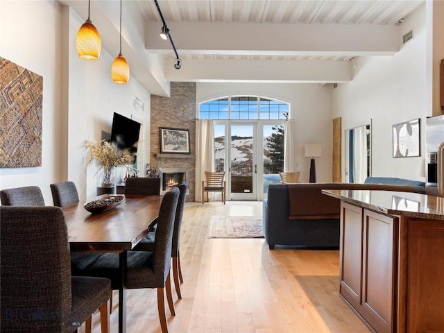 dining area with visible vents, beam ceiling, a stone fireplace, rail lighting, and light wood finished floors