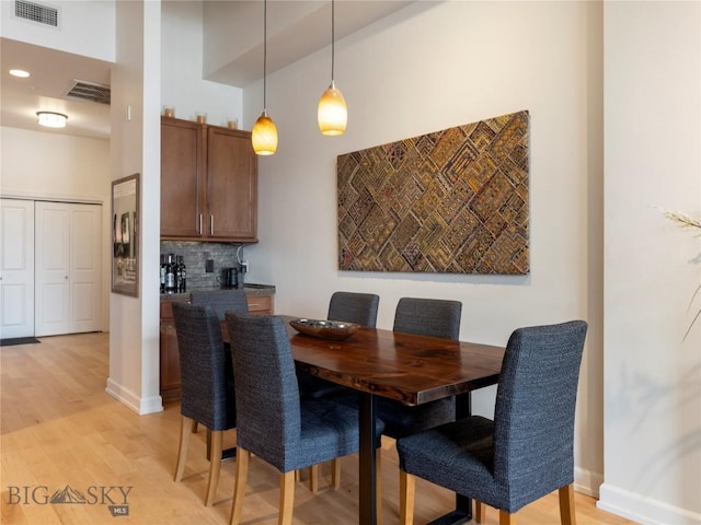 dining area with light wood-style floors, visible vents, a towering ceiling, and baseboards