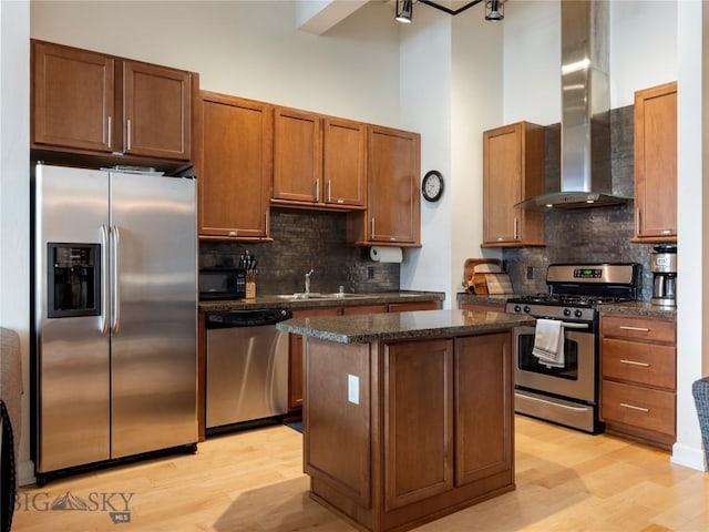 kitchen with a high ceiling, a sink, stainless steel appliances, wall chimney range hood, and a center island