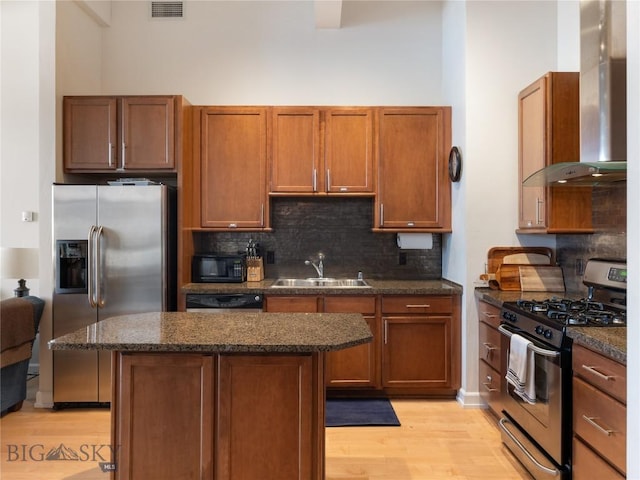 kitchen with tasteful backsplash, light wood-style flooring, appliances with stainless steel finishes, wall chimney exhaust hood, and a sink