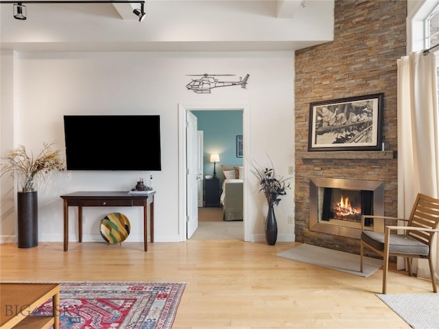 living area featuring a stone fireplace, baseboards, and wood finished floors