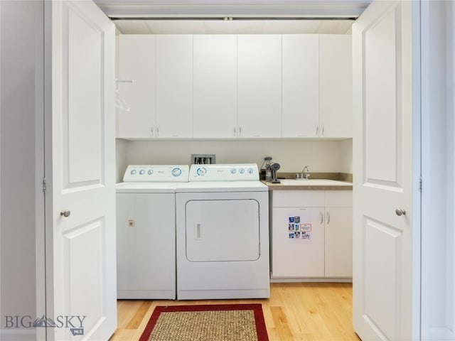 clothes washing area featuring washing machine and dryer, cabinet space, light wood-type flooring, and a sink