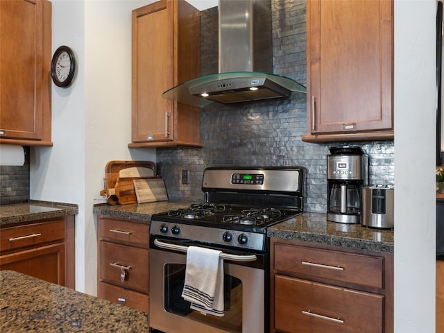 kitchen featuring tasteful backsplash, stainless steel range with gas cooktop, brown cabinets, and wall chimney exhaust hood