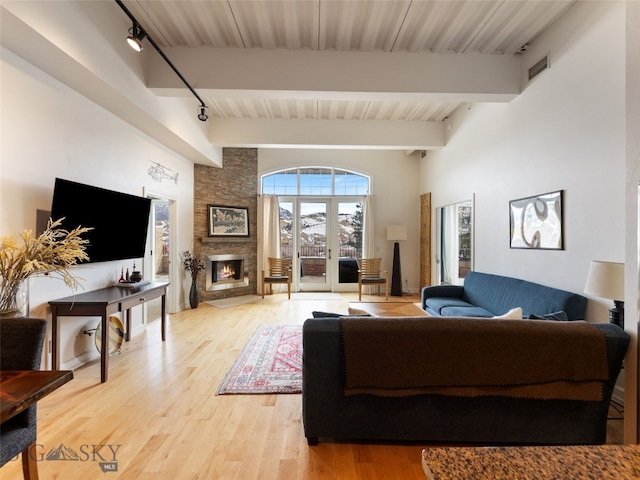 living room featuring light wood-type flooring, beam ceiling, a stone fireplace, and rail lighting