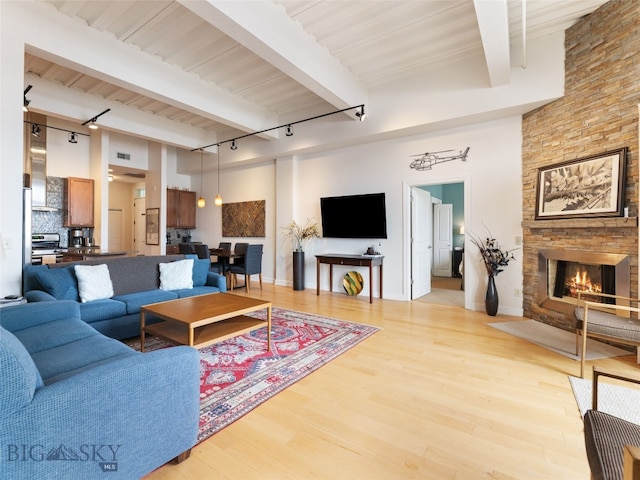 living room featuring light wood-type flooring, beam ceiling, a towering ceiling, and a fireplace