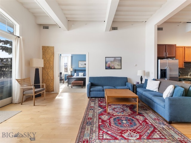 living area with beamed ceiling, visible vents, and light wood finished floors