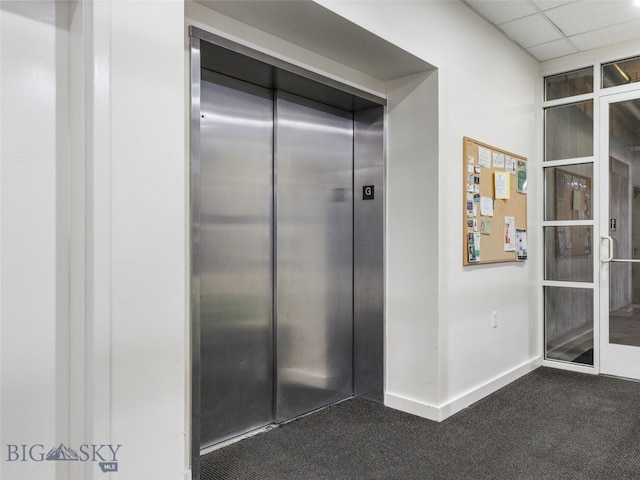 hall featuring elevator, dark carpet, a paneled ceiling, and baseboards