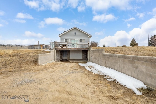 rear view of house with a deck, fence, a garage, and dirt driveway