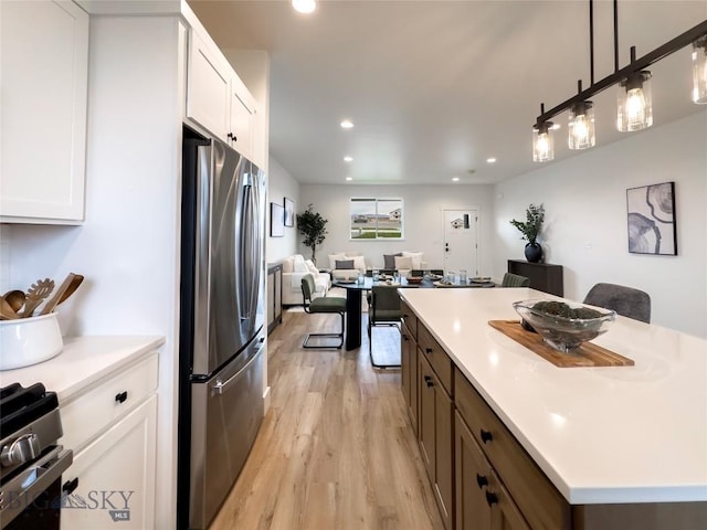 kitchen featuring stainless steel appliances, light countertops, white cabinets, light wood-style floors, and open floor plan