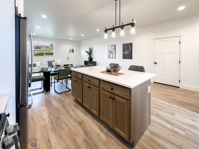 kitchen with light wood-type flooring, a center island, freestanding refrigerator, recessed lighting, and light countertops