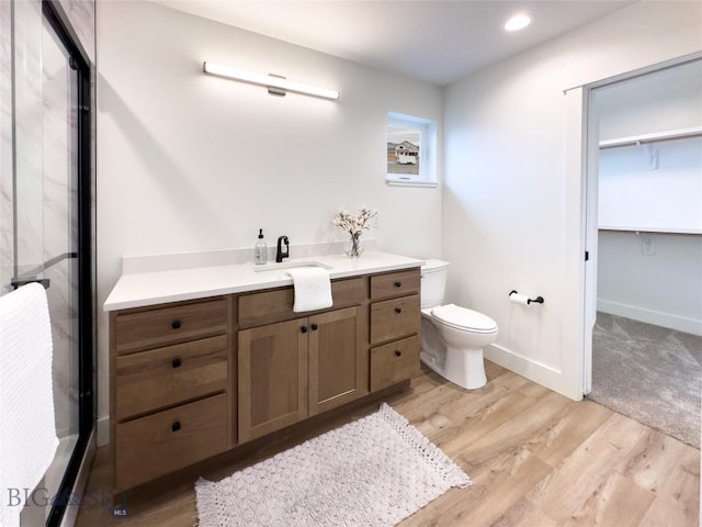 full bath with baseboards, toilet, wood finished floors, a shower with shower door, and vanity