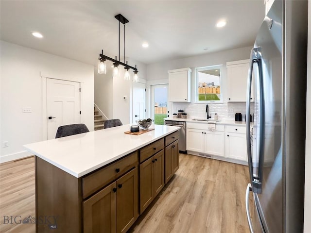 kitchen featuring backsplash, light wood-type flooring, appliances with stainless steel finishes, white cabinets, and a sink