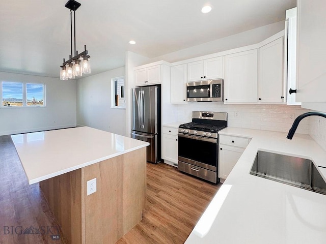 kitchen with light wood finished floors, a sink, light countertops, appliances with stainless steel finishes, and tasteful backsplash