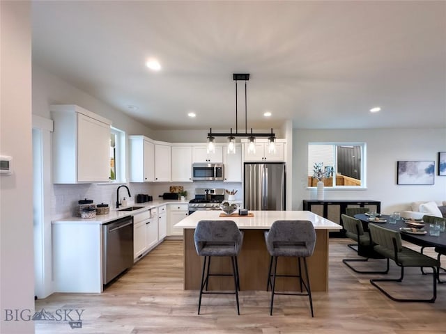 kitchen with a breakfast bar, a sink, a center island, white cabinetry, and appliances with stainless steel finishes