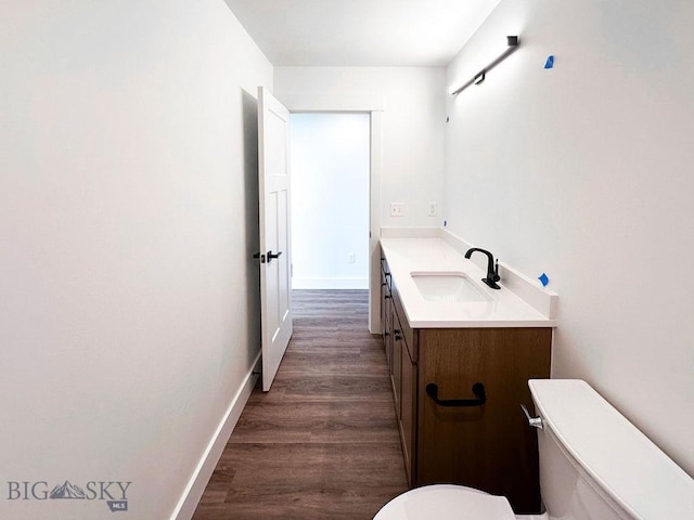 bathroom featuring baseboards, toilet, wood finished floors, and vanity