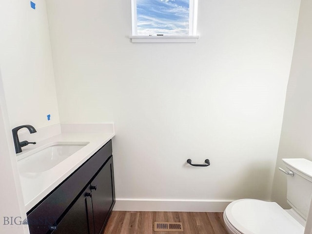 half bath with visible vents, toilet, wood finished floors, baseboards, and vanity