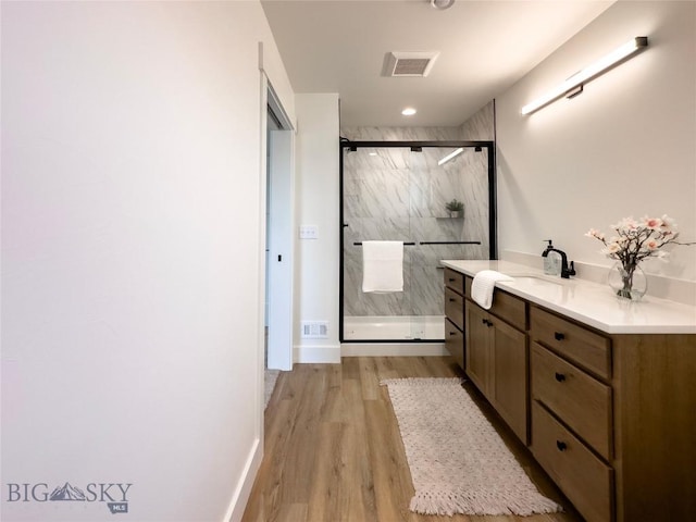 bathroom with a marble finish shower, visible vents, vanity, and wood finished floors