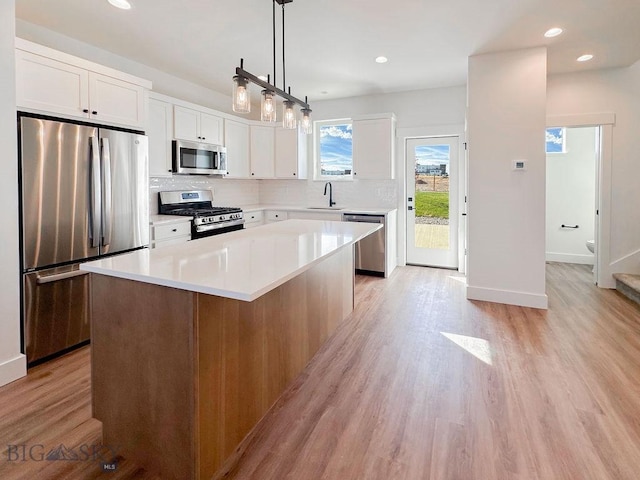 kitchen with a kitchen island, a sink, stainless steel appliances, white cabinetry, and light wood-type flooring