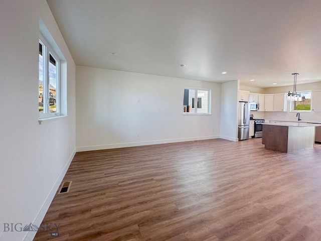 unfurnished living room featuring wood finished floors, visible vents, baseboards, recessed lighting, and a sink