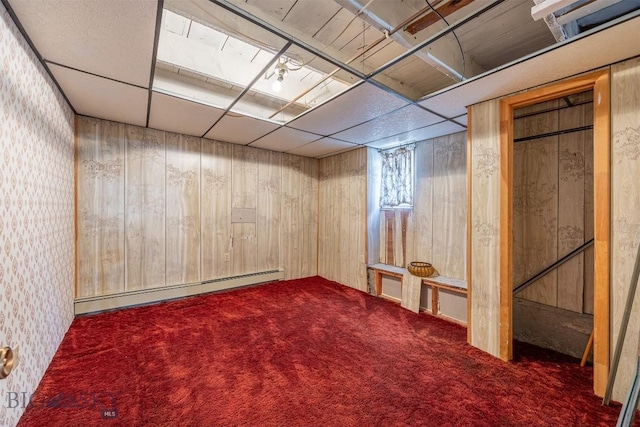 below grade area with wooden walls, a paneled ceiling, carpet, and a baseboard radiator