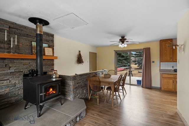 dining area with a wood stove, light wood-style floors, and ceiling fan