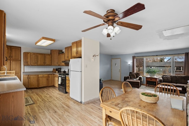 kitchen with brown cabinetry, freestanding refrigerator, light wood-style floors, stainless steel gas range oven, and tasteful backsplash