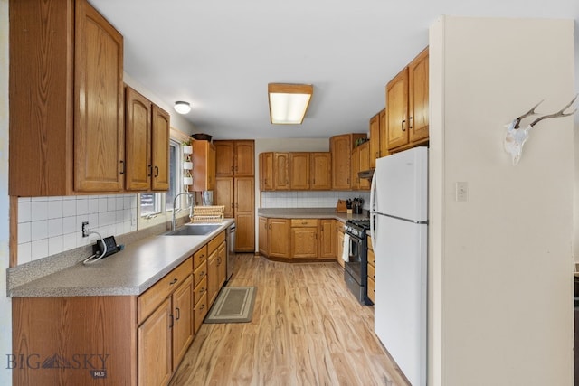 kitchen featuring a sink, gas range, light wood-style flooring, freestanding refrigerator, and stainless steel dishwasher