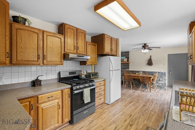 kitchen with backsplash, under cabinet range hood, light wood-style flooring, freestanding refrigerator, and gas stove