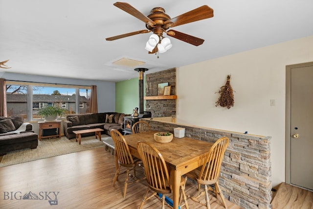 dining area with ceiling fan, wood finished floors, and a wood stove